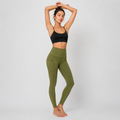A woman modeling high-waisted olive green leggings and a black sports bra against a light gray studio background.