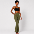 A woman modeling high-waisted olive green flare leggings with a black sports bra against a light gray studio background.