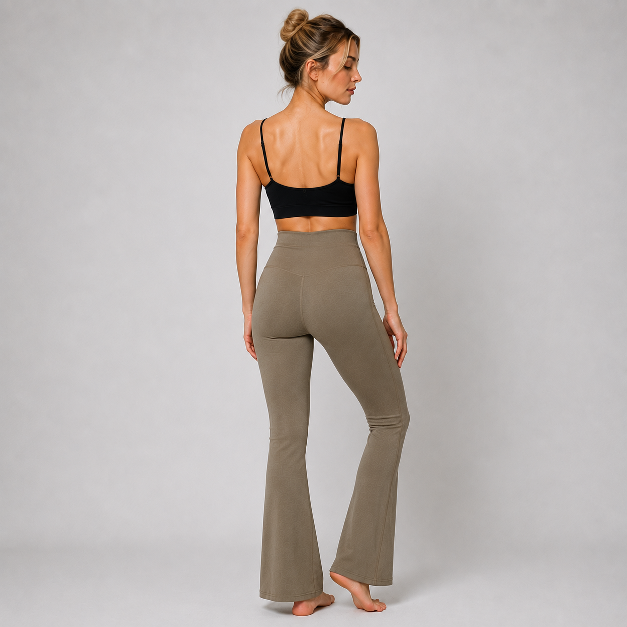 A woman shown from the back wearing a black sports bra and high-waisted, flared olive-brown pants against a light gray studio background.